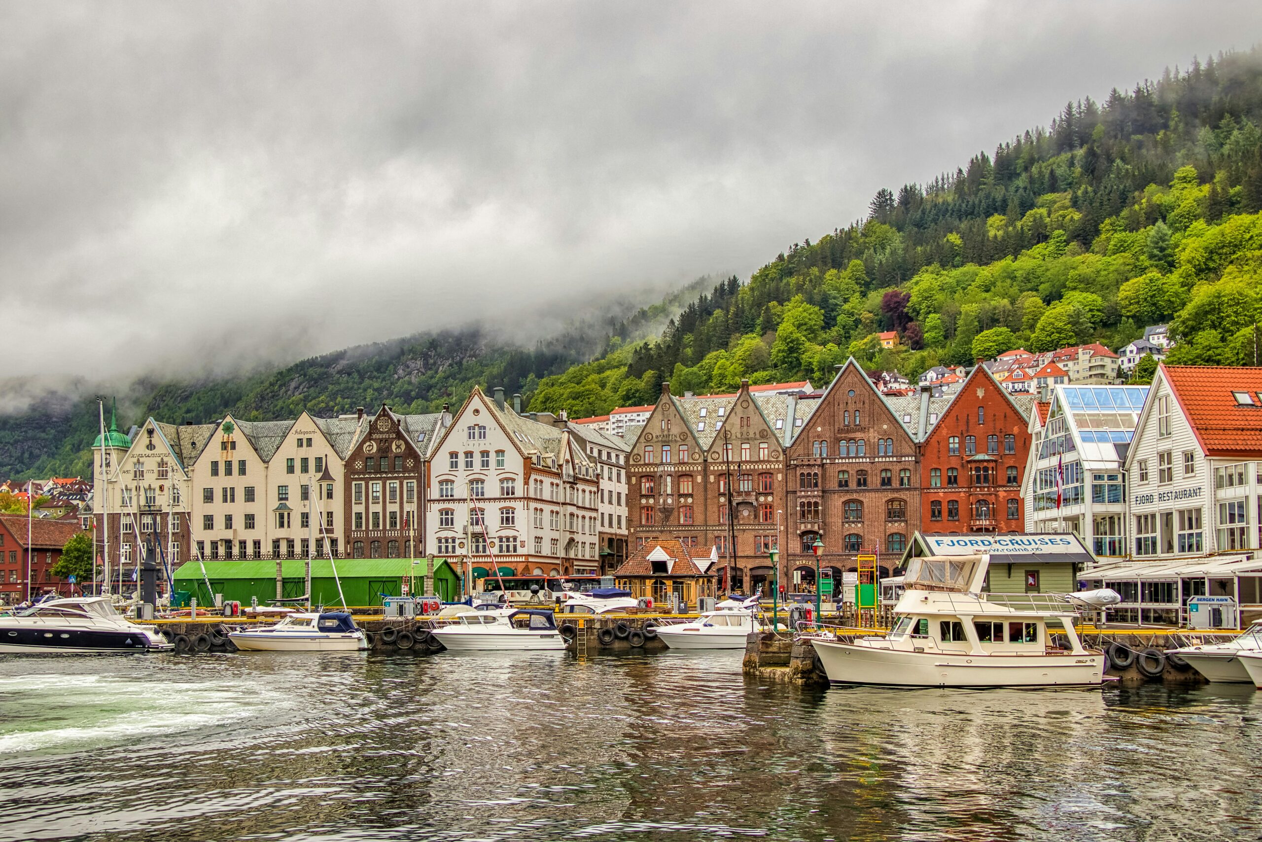 Scenic view of Bryggen's colorful buildings and boats on a cloudy day in Bergen, Norway.