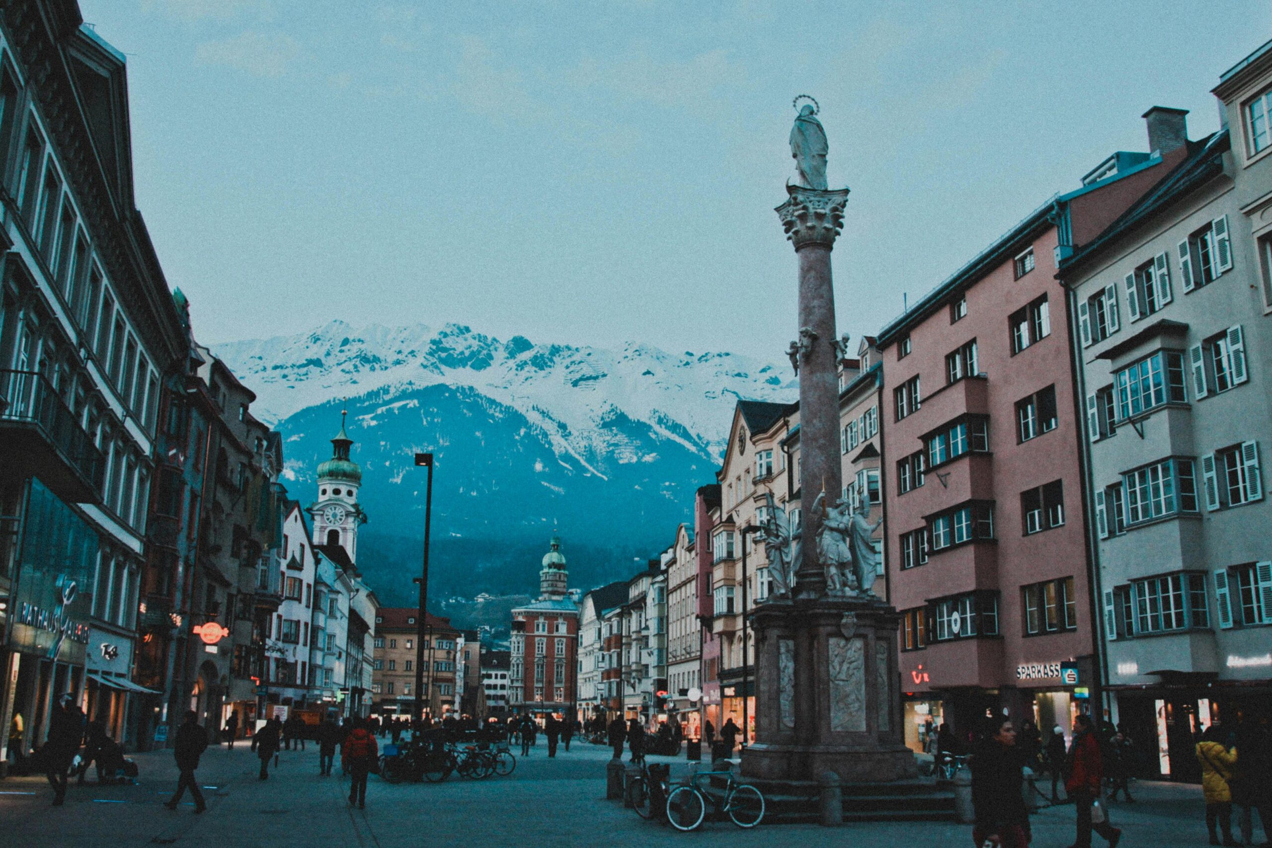 Bustling street in Innsbruck, Austria, with historical buildings and the Alps in the background.