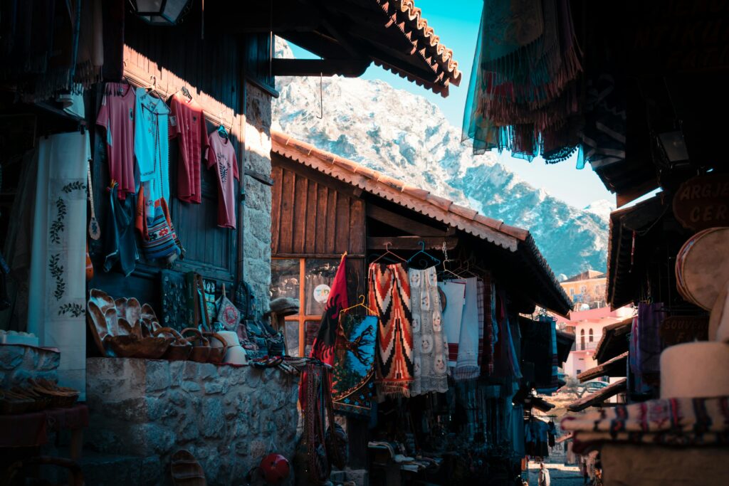 Explore vibrant textiles and crafts in the market of Krujë with a stunning mountain backdrop.