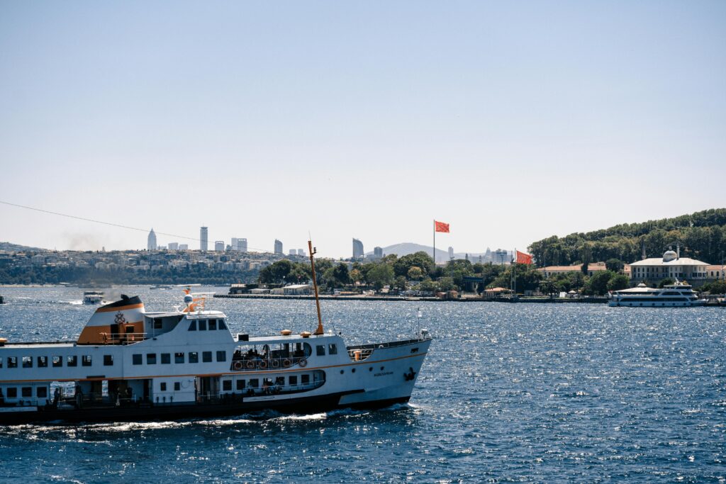 A ferry cruises the Bosphorus with Istanbul skyline in the background under a clear blue sky.