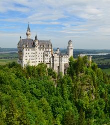 Capture of iconic Neuschwanstein Castle surrounded by vibrant green forest in Bavarian landscape.